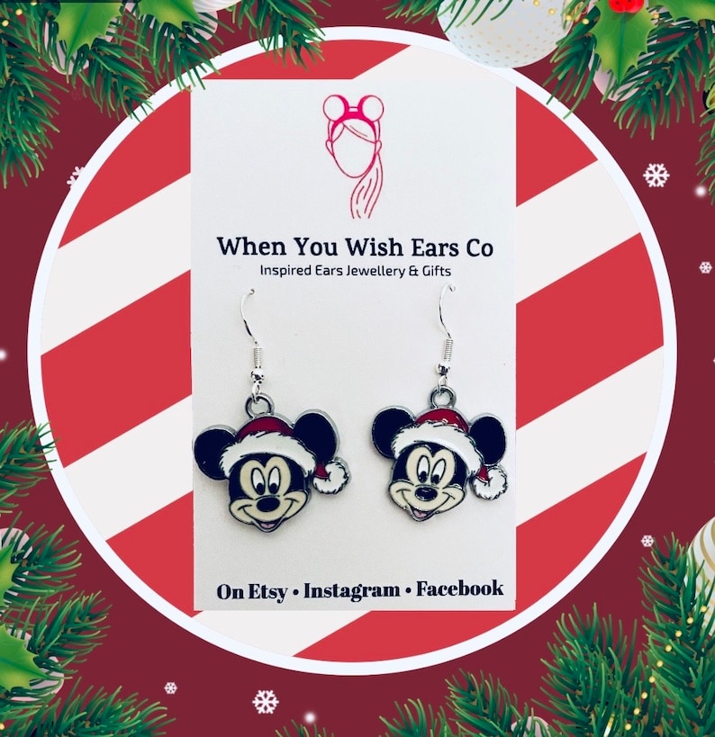 May include: A pair of silver dangle earrings featuring a cartoon Mickey Mouse wearing a Santa hat. The earrings are on a white card with the text "When You Wish Ears Co Inspired Ears Jewellery & Gifts On Etsy Instagram Facebook".