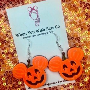May include: Orange pumpkin-shaped Mickey Mouse earrings with a jack-o'-lantern face. The earrings are on a white card with the text "When You Wish Ears Co. Inspired Ears Jewellery & Gifts".