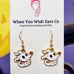 May include: Gold-tone earrings featuring a white enamel Zero from The Nightmare Before Christmas. The earrings are on a white card with the text "When You Wish Ears Co. Inspired Ears Jewellery & Gifts. On Etsy, Instagram, Facebook."