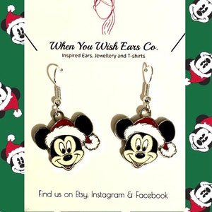 May include: Silver dangle earrings featuring a Mickey Mouse head wearing a Santa hat. The earrings are on a white background with the text "When You Wish Ears Co. Inspired Ears, Jewellery and T-shirts" and "Find us on Etsy. Instagram & Facebook".