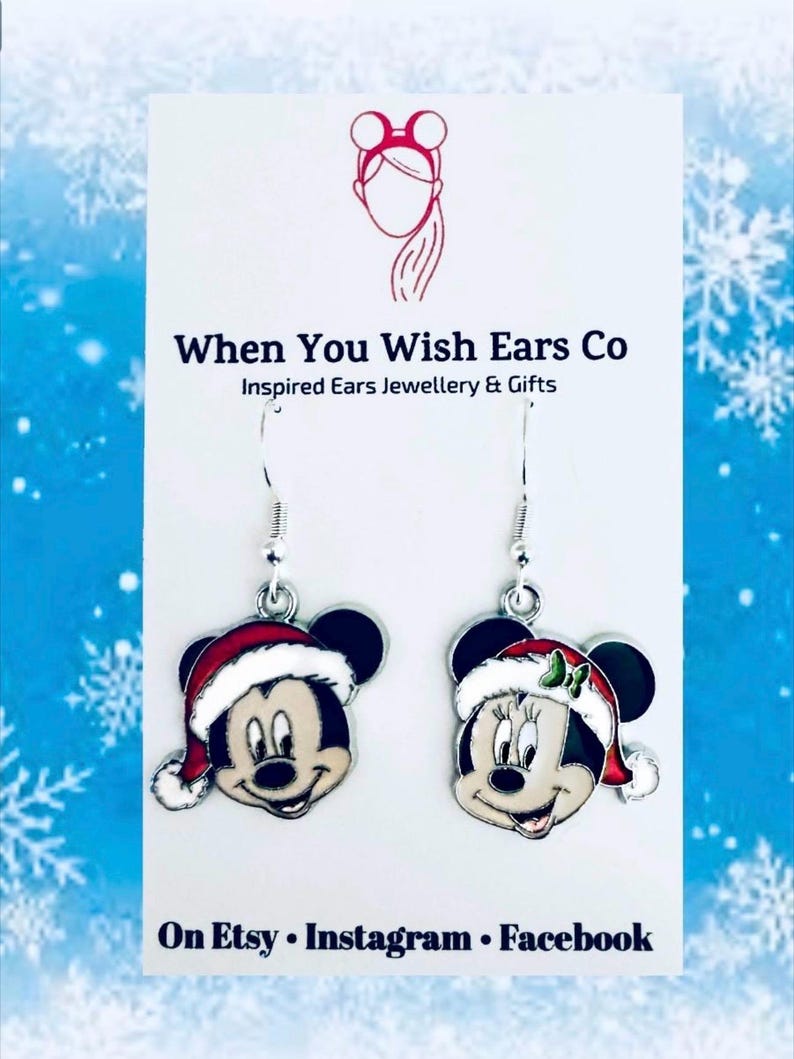 May include: A pair of silver dangle earrings featuring a Christmas-themed Mickey Mouse and Minnie Mouse. Mickey is wearing a red Santa hat with white trim and Minnie is wearing a red Santa hat with white trim and a green bow. The earrings are on a white card with the text "When You Wish Ears Co Inspired Ears Jewellery & Gifts On Etsy Instagram Facebook".