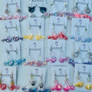 May include: Assortment of colorful glitter filled Mickey Mouse ear earrings. The earrings are made of clear plastic and feature different glitter colors and designs.  Find us on Instagram & Facebook.