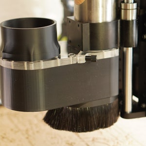 May include: A black dust collection shroud with a clear plastic dust shield and a black brush attached to the bottom. The shroud is mounted on a silver metal spindle.
