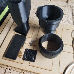 May include: A set of five black 3D printed parts for a dust collection system. The parts include a large rectangular piece, a smaller rectangular piece, a round piece with a hole in the center, a round piece with a lip, and a round piece with a lip and a hole in the center.