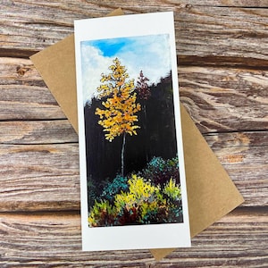 May include: A rectangular greeting card featuring an acrylic painting of a single tall tree with vibrant yellow autumn leaves standing against a dark forest background, with a bright blue sky above and colorful low-lying foliage in the foreground.