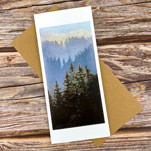May include: A rectangular greeting card featuring a vertical painting of a dense forest with dark green pine trees in the foreground and a misty, light blue mountain range in the background, set against a plain white border frame.