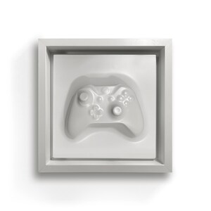 Puede incluir: Una imagen enmarcada en blanco con un mando de videojuego en 3D blanco en su interior.