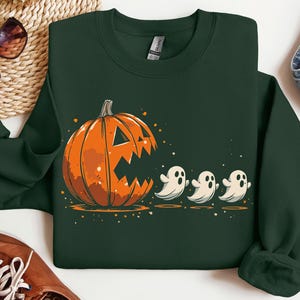 May include: Dark green sweatshirt with a Halloween design. The graphic shows a large orange pumpkin with a carved face and three small white ghosts. The sweatshirt is made of a soft material.
