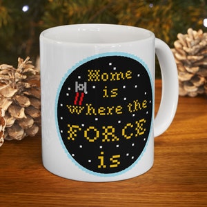 May include: White ceramic mug with a black circle design featuring a pixelated spaceship and the text "Home is where the FORCE is".