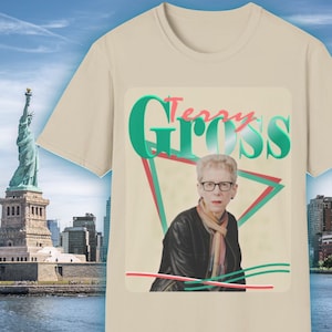 May include: A beige t-shirt with a retro-style graphic design featuring a woman's face and the text "Terry Gross" in green and red letters.