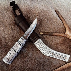 May include: A fixed-blade knife with a textured metal blade and a white handle featuring a black woven pattern. The knife is paired with a dark brown leather sheath that has a matching white handle section with a black woven pattern.