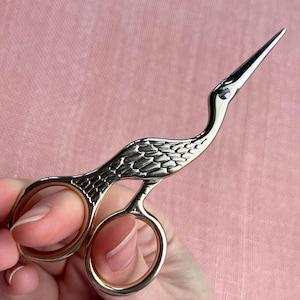 Peut inclure: Une paire de ciseaux à broder argentés en forme de grue. Les ciseaux présentent un motif détaillé sur le corps de la grue et une pointe acérée. Les trous pour les doigts sont de couleur dorée.