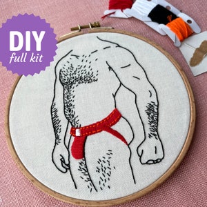 Op de afbeelding: DIY borduurpakket met een gestileerde mannelijke figuur in een rode jockstrap, geborduurd op witte stof in een houten hoepel. De tekst "DIY full kit" staat in een paarse ster. Borduurgaren en naald zijn inbegrepen.