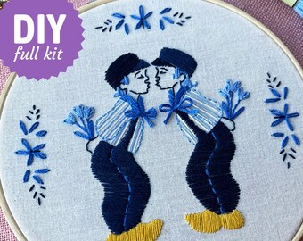 May include: Embroidered DIY full kit featuring two figures in traditional Dutch attire kissing, holding blue flowers. The design is stitched in shades of blue and yellow on a white fabric, framed by a wooden hoop. The kit includes the text "DIY full kit".