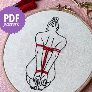 May include: Embroidered hoop art featuring a line drawing of a person with their arms tied behind their back with red thread.