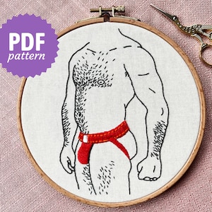 May include: Embroidered design of a hairy torso wearing a red jockstrap, in a wooden embroidery hoop.