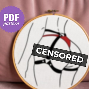 May include: A black and white embroidery hoop with a line drawing of a person wearing a harness. The harness is black with red accents. The word "CENSORED" is written across the image.