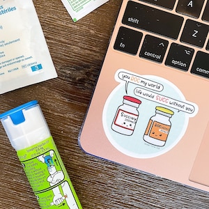 Może przedstawiać: Naklejka z jasnoniebieskim tłem przedstawiająca dwie kreskówkowe fiolki z twarzami. Tekst "you ROC my world life would SUCC without you" jest napisany w dymku nad fiolkami. Naklejka znajduje się na różowym laptopie.