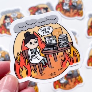 Peut inclure: Un autocollant représentant une illustration de dessin animé d'un médecin assis à un bureau avec un ordinateur portable et une pile de papiers. Le bureau est en feu et il y a de la fumée au-dessus de la tête du médecin. Le texte "This is fine." est dans une bulle de dialogue au-dessus de la tête du médecin. L'autocollant est sur un fond blanc.