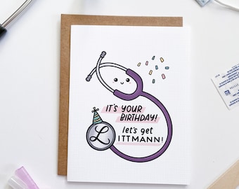 Puede incluir: Una tarjeta blanca con un estetoscopio de dibujos animados morado que lleva un gorro de fiesta. La tarjeta dice "¡Es tu cumpleaños! ¡Vamos a celebrarlo!"
