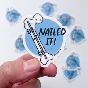 May include: A white sticker featuring a cartoon femur bone illustration and the text "Nailed It!" in black. The bone is set against a light blue circle. Several other stickers with the same design are visible in the background.