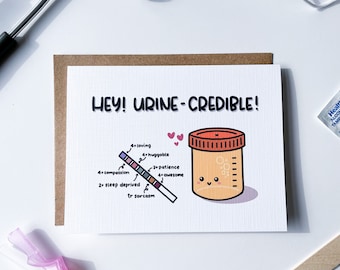May include: A humorous greeting card with the text "HEY! URINE-CREDIBLE!" and a cartoon illustration of a urine sample container with a smiling face. The container has a scale on the side and a urine test strip with different colored sections labeled with personality traits like "loving", "huggable", "patience", "awesome", "compassion", "sleep deprived", and "sarcasm".