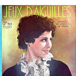 May include: A vintage magazine cover featuring a woman with short, dark hair wearing a white lace collar. The magazine is titled "Jeux d'Aiguilles" and the cover text also includes "La Mode, La Lingerie, Le Home." The magazine is dated "N° 21 Mai 1936".