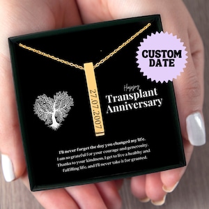 May include: A gold necklace with a vertical bar pendant engraved with the date "27.07.2007". The necklace is in a black box with the words "Happy Transplant Anniversary" and a message about gratitude for a life-changing event.