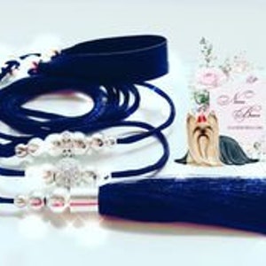 May include: A collection of dark blue hair accessories, including a headband, several beaded hair ties, and a tassel. A small decorative Yorkie figurine and a floral-themed card are also present.