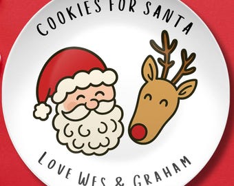 May include: White ceramic plate with a Santa Claus and reindeer design. The plate has the text "COOKIES FOR SANTA" at the top and "LOVE WES & GRAHAM" at the bottom. Festive Christmas themed plate.