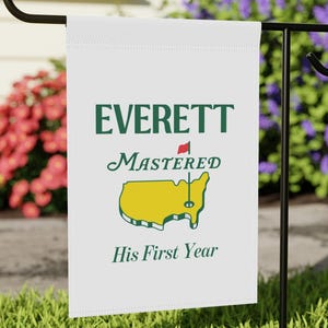 Op de afbeelding: Witte tuin vlag met de tekst "EVERETT MASTERED His First Year" en een groene en gele afbeelding van de Verenigde Staten met een rode vlag.