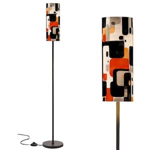 May include: A tall floor lamp with a black metal frame and a cylindrical lampshade. The lampshade features a geometric pattern of orange, black, and gray squares and rectangles. The lamp has a round base and a foot switch.