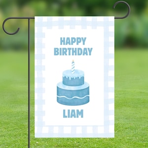 May include: A blue and white garden flag with a blue birthday cake and a single lit candle. The text "Happy Birthday" and the name "Liam" are printed on the flag.