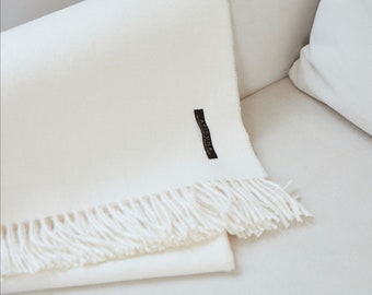 May include: A white throw blanket with a fringe border and a black label that says "Apresuna" on a white couch.