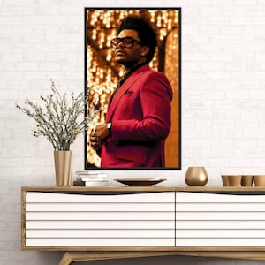 May include: A man in a red suit and black-rimmed glasses stands in front of a blurred background of golden lights.