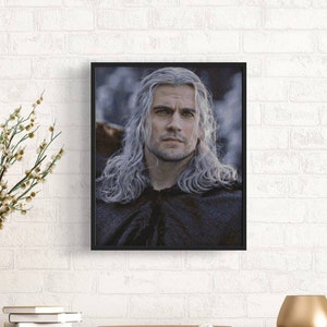 May include: A framed portrait of a man with long, white hair and a beard. He is wearing a dark hooded cloak and has a serious expression on his face.