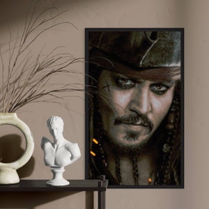 Puede incluir: Un retrato enmarcado de Jack Sparrow de la serie de películas Piratas del Caribe. La imagen presenta un primer plano del rostro del personaje, con un tatuaje de cruz y una mirada intensa. El retrato está en un marco negro.