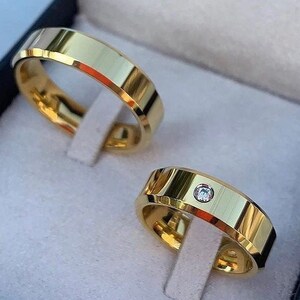 Puede incluir: Dos alianzas de oro, una con un pequeño diamante, en una caja de terciopelo negro.