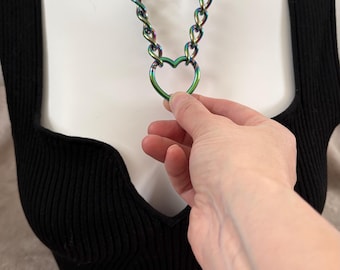 May include: A black choker necklace with a silver chain and a heart-shaped charm. The chain is iridescent with rainbow colors.