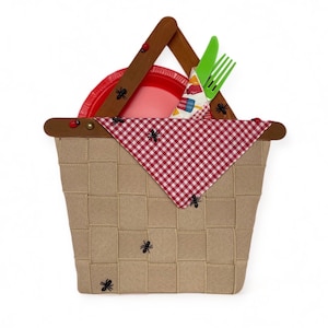 May include: A brown wicker picnic basket with a red and white checkered cloth lining. The basket has a wooden handle and is decorated with black ants. A red plastic plate and green plastic utensils are inside the basket.