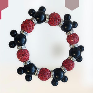 Puede incluir: Un brazalete negro y rojo con dijes de cabeza de Mickey Mouse y cuentas de diamantes de imitaci&oacute;n rojos.