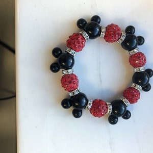 Puede incluir: Un brazalete de cuentas rojas y negras con dijes de cabeza de Mickey Mouse. Las cuentas est&aacute;n cubiertas de diamantes de imitaci&oacute;n.