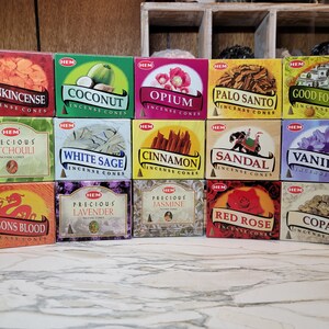 May include: Assortment of 14 HEM incense cones in various scents, including Frankincense, Coconut, Opium, Palo Santo, Good Fortune, Precious Patchouli, White Sage, Cinnamon, Sandal, Vanilla, Dragons Blood, Precious Lavender, Precious Jasmine, Red Rose, and Copal. The cones are arranged in four rows of three and one row of two, with the HEM logo on each box.