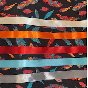 May include: A fabric with a black background featuring a colorful feather pattern in shades of red, orange, and teal. Horizontal ribbons in white, orange, red, light blue, and silver are layered across the fabric.