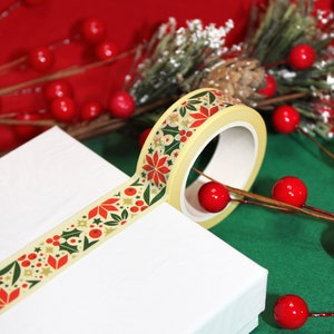 May include: A roll of washi tape with a Christmas-themed design featuring red poinsettias, green holly leaves, and gold stars on a cream background.