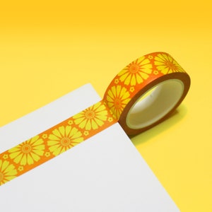 May include: A roll of orange and yellow washi tape with a floral pattern. The tape is on a white surface and a yellow background.