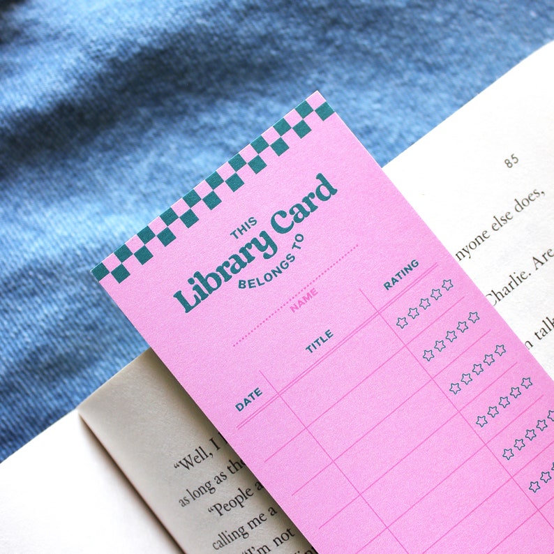 May include: Pink library card with a checkered green and white design at the top. The card has spaces to fill in the name, title, date, and rating of a book. The rating is indicated by a row of five stars.