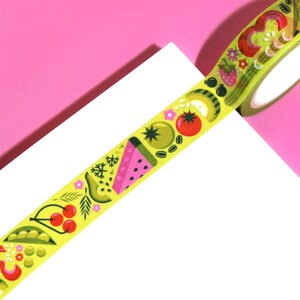 May include: A roll of yellow washi tape with a repeating pattern of colorful fruits and vegetables. The tape features watermelon, kiwi, avocado, cherries, peas, and tomatoes.
