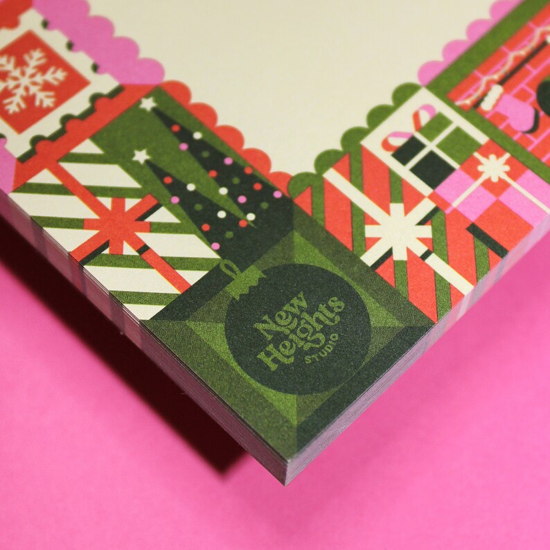 Peut inclure: Une pile de papeterie avec un motif de No&euml;l festif. La bordure pr&eacute;sente des bo&icirc;tes cadeaux, des sapins de No&euml;l et des flocons de neige en rouge, vert et rose. Le coin inf&eacute;rieur affiche une d&eacute;coration verte avec le texte "New Heights Studio".