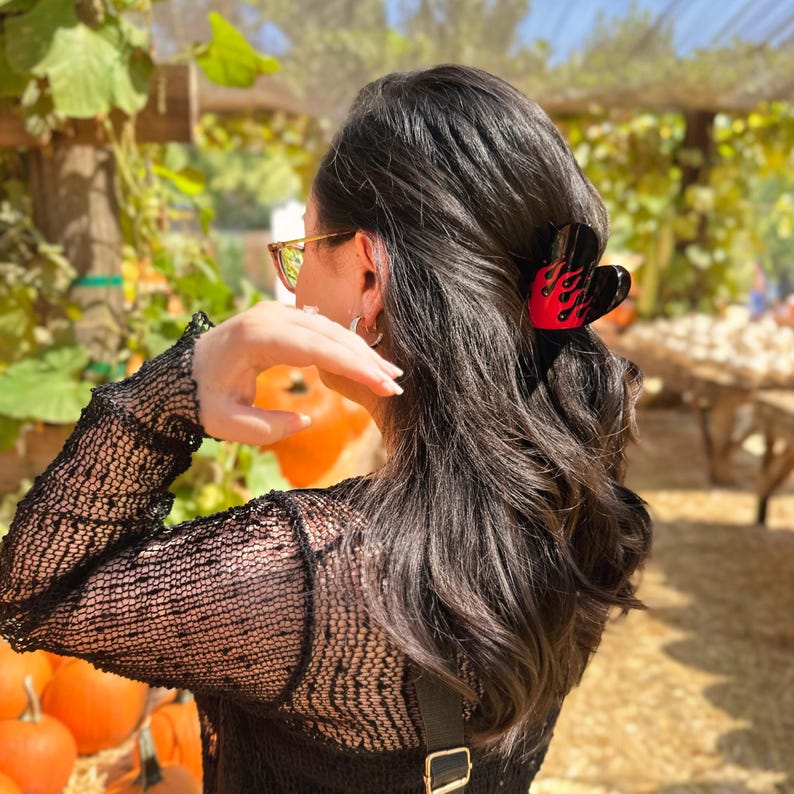 Model in a pumpkin patch field, with half-up-half-down hairdo, clipped up by red and black colored heart and flame hair claw on dark hair.